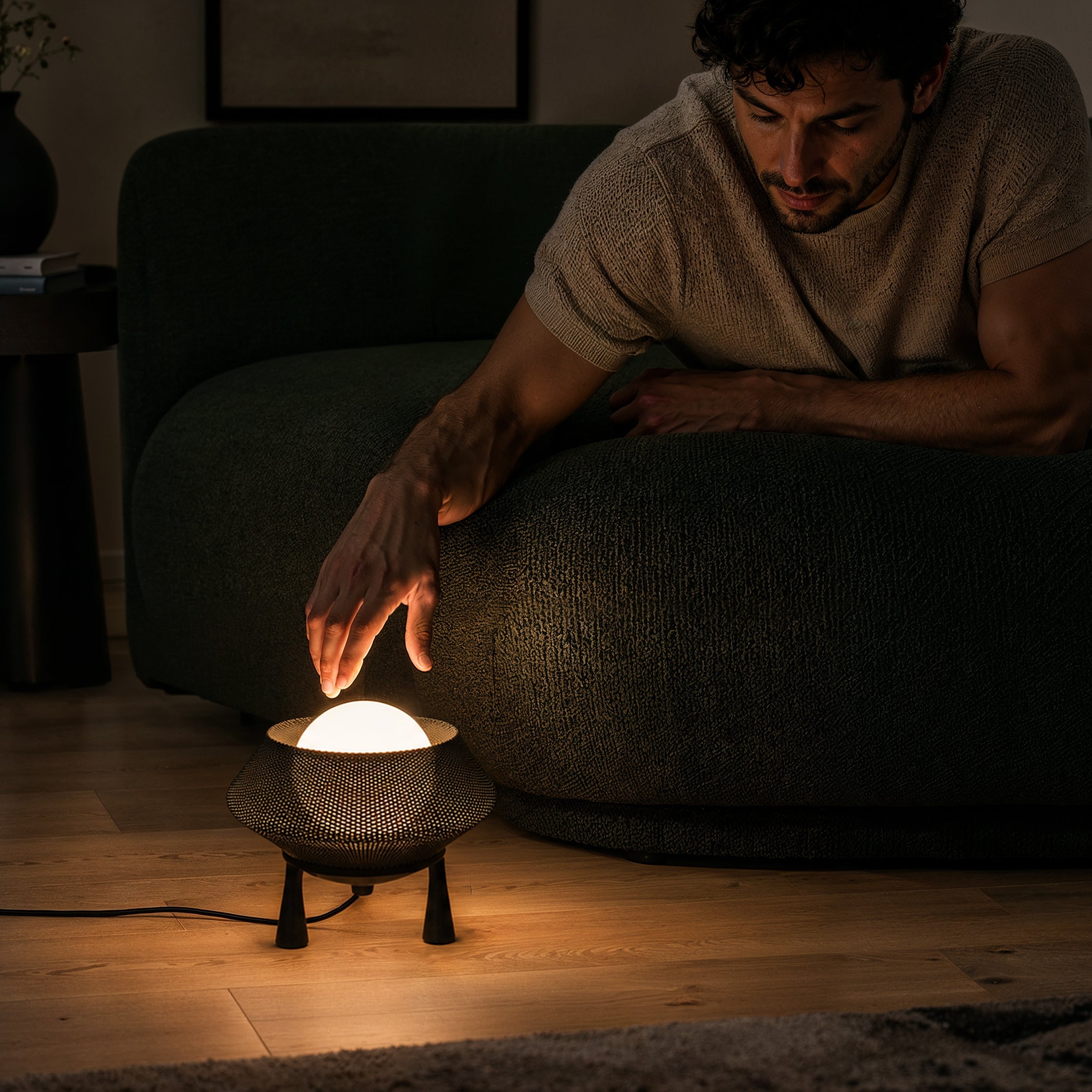 Halo lamp glowing warmly on a light wood floor beside a curved beige sofa in a dim modern living room, creating a cozy ambient atmosphere.