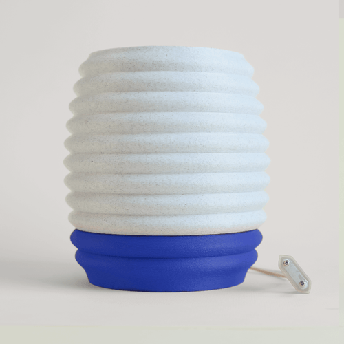 Cylindrical lamp with white stacked design and blue base on a light beige background